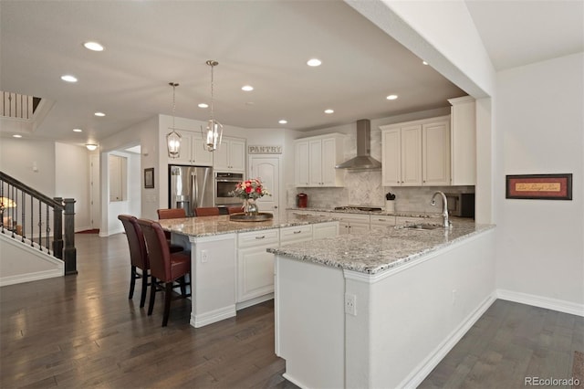 kitchen featuring wall chimney range hood, stainless steel appliances, dark hardwood / wood-style flooring, white cabinets, and sink