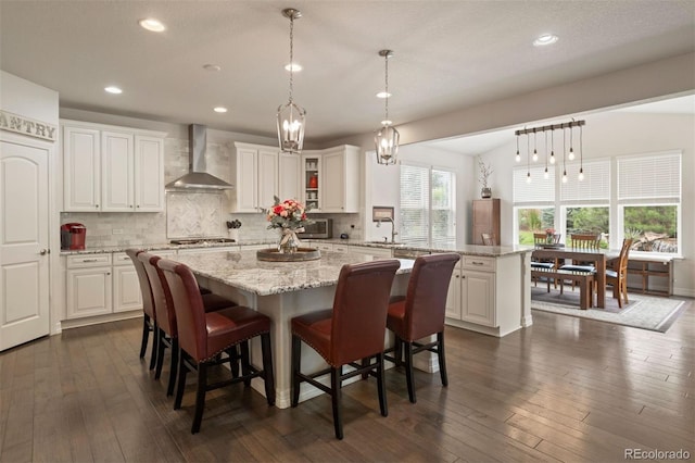 kitchen with white cabinets, dark hardwood / wood-style floors, decorative backsplash, and wall chimney range hood