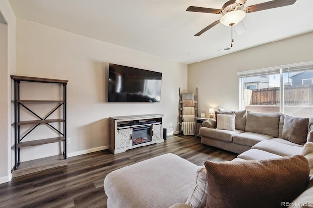 living area with visible vents, baseboards, a ceiling fan, a glass covered fireplace, and dark wood-style flooring