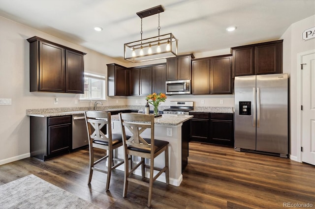 kitchen with dark wood-style flooring, pendant lighting, stainless steel appliances, dark brown cabinetry, and a kitchen island