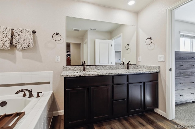 full bathroom featuring double vanity, visible vents, wood finished floors, a garden tub, and a sink