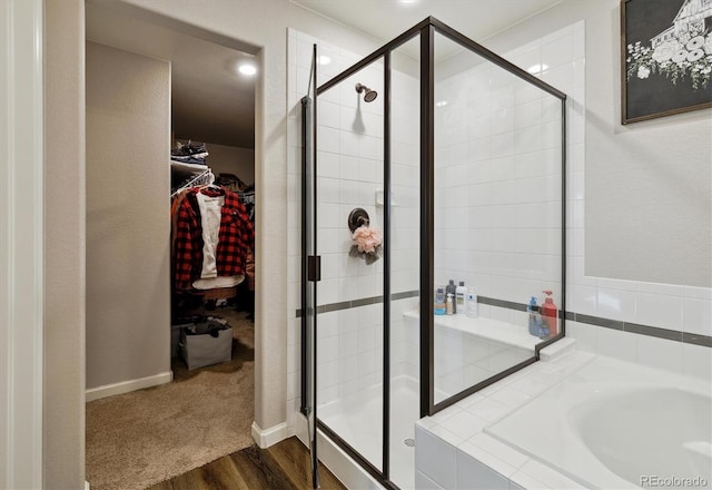 full bathroom with wood finished floors, baseboards, a spacious closet, a shower stall, and a bath