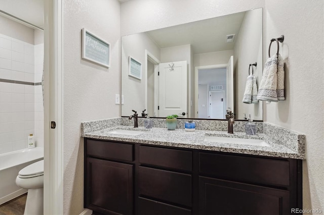 full bath featuring double vanity, toilet, a sink, and a textured wall