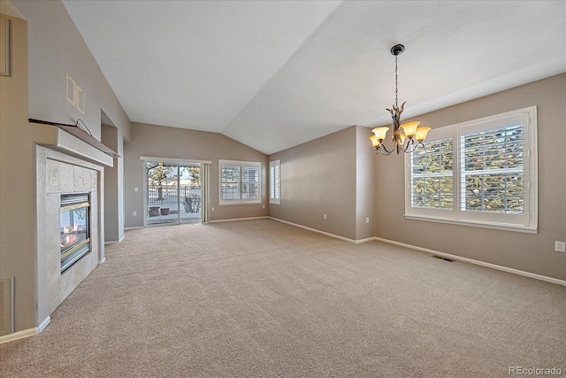 unfurnished living room featuring a tiled fireplace, lofted ceiling, carpet flooring, and an inviting chandelier