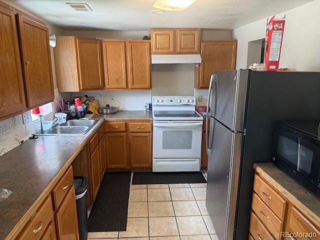 449 Lowell Blvd, Denver, CO 80204 - kitchen featuring white electric range oven, under cabinet range hood, black microwave, light tile patterned floors, and freestanding refrigerator