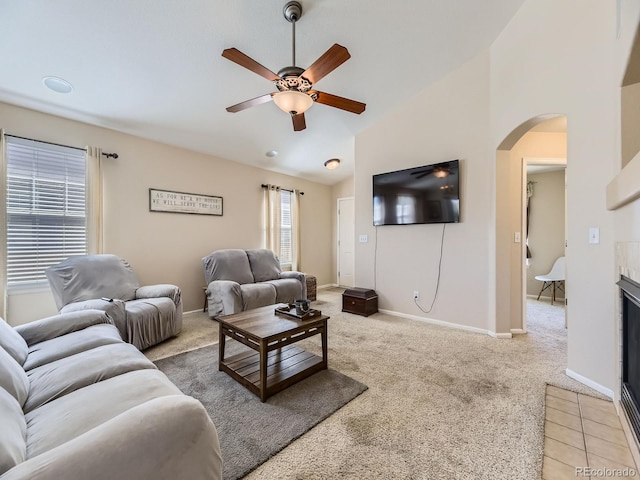 living room featuring baseboards, arched walkways, ceiling fan, vaulted ceiling, and light carpet