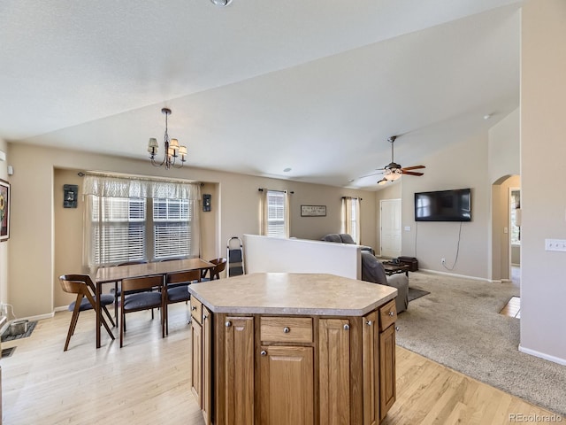 kitchen with a center island, arched walkways, brown cabinetry, lofted ceiling, and hanging light fixtures