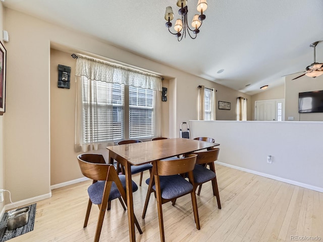 dining space with light wood finished floors, ceiling fan with notable chandelier, baseboards, and vaulted ceiling