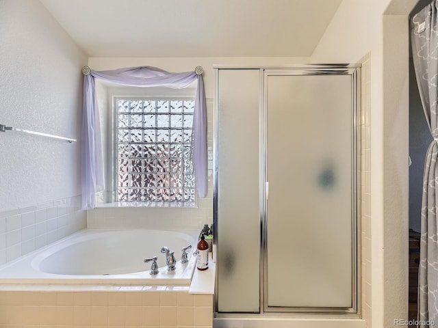 bathroom featuring a bath, a shower stall, and a textured wall