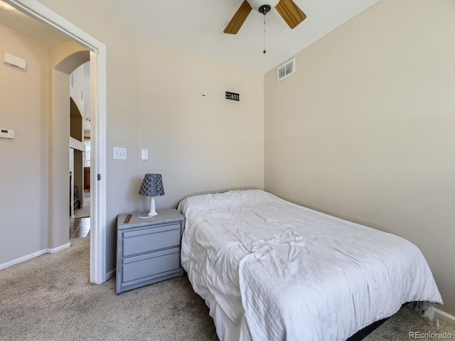 carpeted bedroom featuring visible vents, arched walkways, baseboards, and ceiling fan