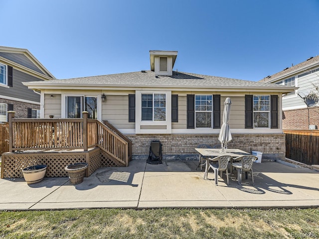 back of property with brick siding, a shingled roof, a patio, and fence