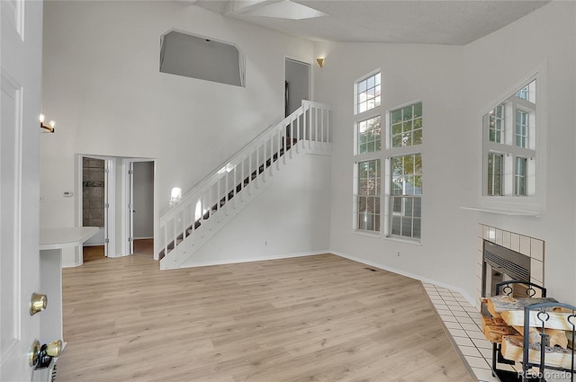 unfurnished living room with a textured ceiling, light wood-type flooring, a fireplace, and a high ceiling