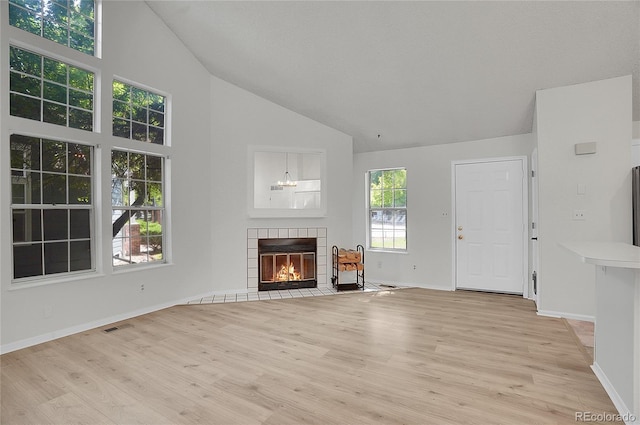 unfurnished living room with a tiled fireplace, high vaulted ceiling, and light wood-type flooring