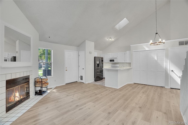 kitchen with a tile fireplace, pendant lighting, light hardwood / wood-style flooring, stainless steel fridge with ice dispenser, and white cabinetry