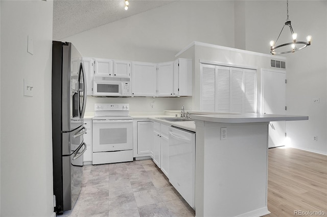 kitchen featuring kitchen peninsula, white appliances, pendant lighting, a notable chandelier, and white cabinetry