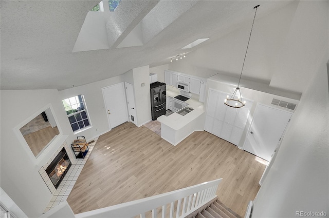 unfurnished living room with a textured ceiling, high vaulted ceiling, a chandelier, light hardwood / wood-style floors, and a tiled fireplace