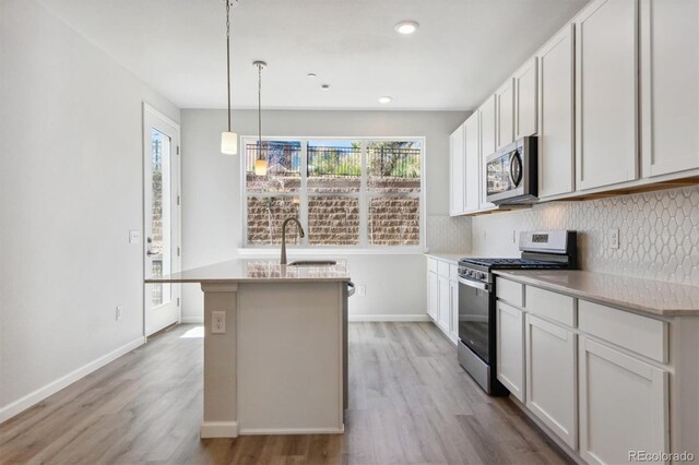 457 Interlocken Blvd Unit 101, Broomfield, CO 80021 - kitchen with appliances with stainless steel finishes, light wood finished floors, a sink, backsplash, and a kitchen island with sink