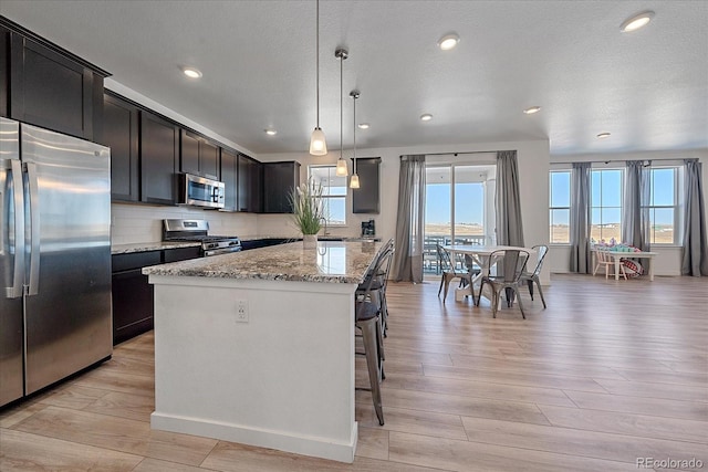 kitchen with hanging light fixtures, light stone counters, light hardwood / wood-style flooring, a kitchen island, and appliances with stainless steel finishes