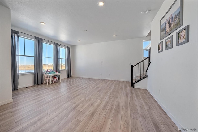 empty room with a textured ceiling, a water view, and light hardwood / wood-style flooring