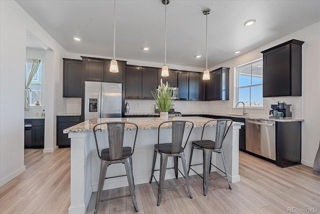 kitchen featuring sink, hanging light fixtures, appliances with stainless steel finishes, a kitchen island, and light wood-type flooring