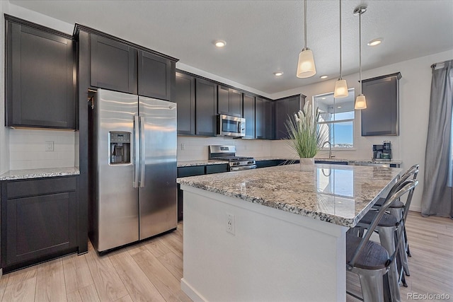 kitchen with pendant lighting, light hardwood / wood-style floors, appliances with stainless steel finishes, tasteful backsplash, and a kitchen island