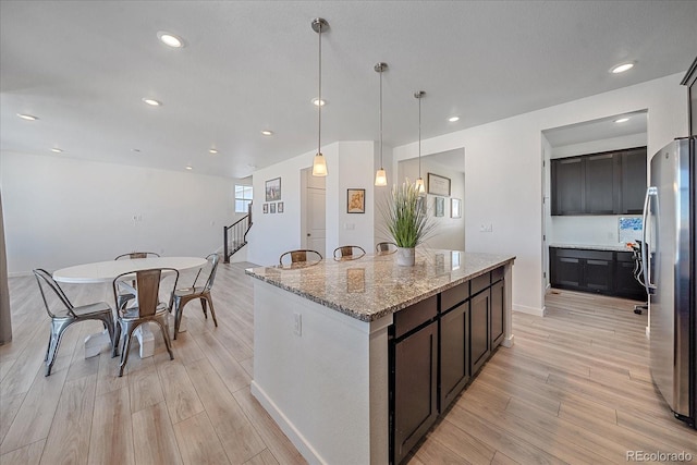 kitchen with stainless steel refrigerator, a center island, light stone counters, light hardwood / wood-style flooring, and decorative light fixtures