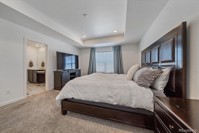 carpeted bedroom with a raised ceiling and connected bathroom