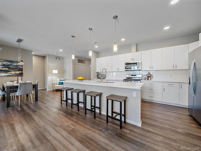 kitchen with appliances with stainless steel finishes, dark hardwood / wood-style flooring, pendant lighting, a center island with sink, and white cabinets