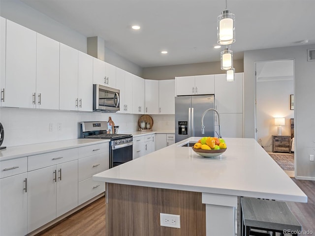 kitchen featuring backsplash, stainless steel appliances, white cabinetry, and an island with sink