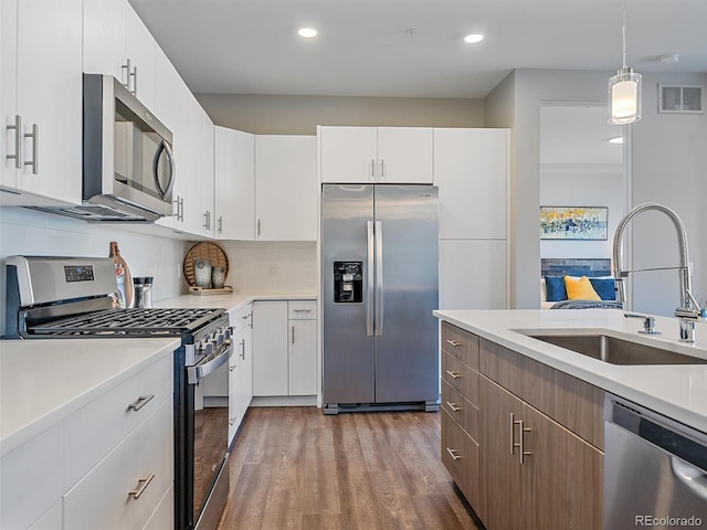 kitchen featuring sink, stainless steel appliances, tasteful backsplash, decorative light fixtures, and white cabinets