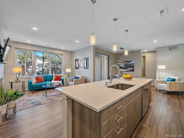 kitchen featuring a kitchen island with sink, sink, stainless steel dishwasher, and dark hardwood / wood-style floors