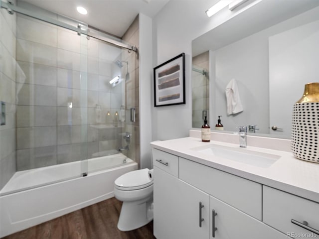 full bathroom featuring hardwood / wood-style floors, vanity, toilet, and bath / shower combo with glass door