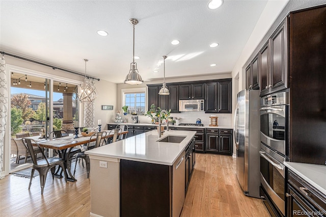 kitchen with light hardwood / wood-style floors, a kitchen island with sink, decorative light fixtures, sink, and appliances with stainless steel finishes