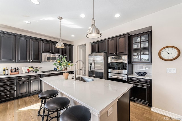 kitchen featuring hanging light fixtures, sink, a kitchen island with sink, stainless steel appliances, and light wood-type flooring