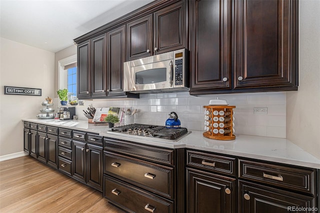 kitchen with light wood-type flooring, light stone countertops, dark brown cabinetry, stainless steel appliances, and backsplash