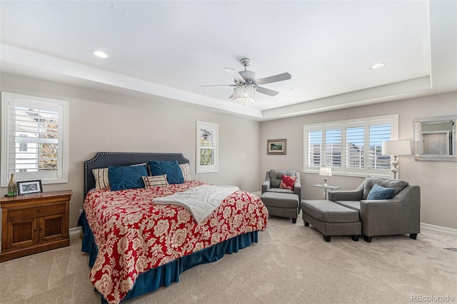 bedroom featuring light carpet, a tray ceiling, multiple windows, and ceiling fan