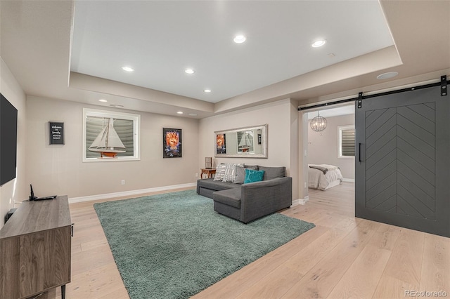 living room featuring light wood-type flooring, a raised ceiling, and a barn door