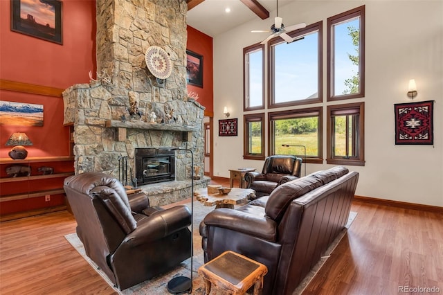 living room with beamed ceiling, a towering ceiling, a stone fireplace, and hardwood / wood-style floors