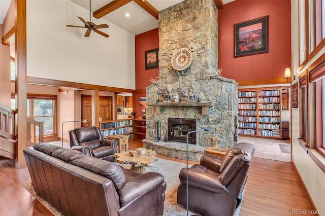 living room featuring a fireplace, light hardwood / wood-style floors, beam ceiling, and a high ceiling