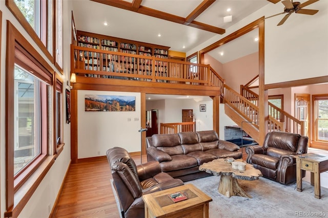 living room featuring ceiling fan, a towering ceiling, light hardwood / wood-style flooring, and beamed ceiling