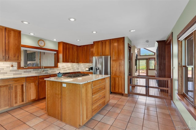 kitchen featuring light tile patterned flooring, sink, tasteful backsplash, a kitchen island, and light stone countertops