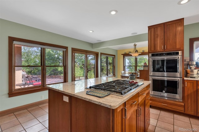 kitchen with appliances with stainless steel finishes, a center island, light tile patterned floors, and light stone counters