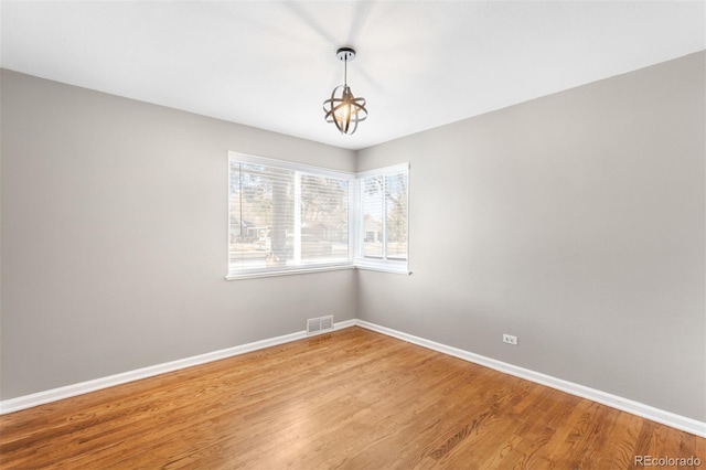 spare room with hardwood / wood-style flooring and a notable chandelier