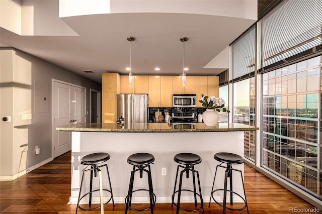 kitchen featuring light brown cabinetry, appliances with stainless steel finishes, dark wood-style flooring, and a kitchen breakfast bar