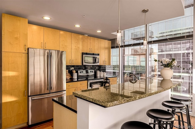 kitchen with a breakfast bar area, stainless steel appliances, hanging light fixtures, decorative backsplash, and dark stone countertops