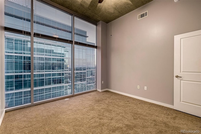 carpeted empty room with floor to ceiling windows, a ceiling fan, visible vents, and baseboards