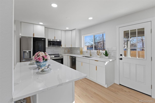 kitchen featuring light stone counters, stainless steel appliances, backsplash, white cabinets, and sink