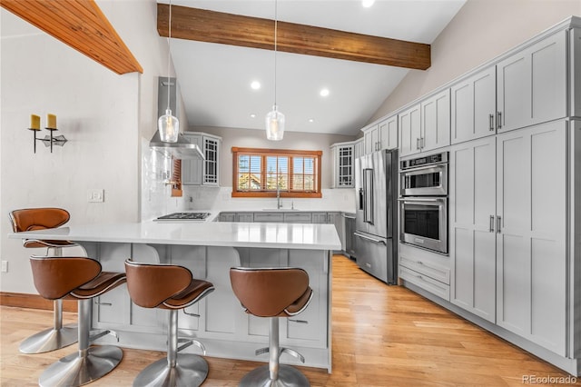 kitchen featuring a peninsula, a sink, stainless steel appliances, glass insert cabinets, and a kitchen breakfast bar