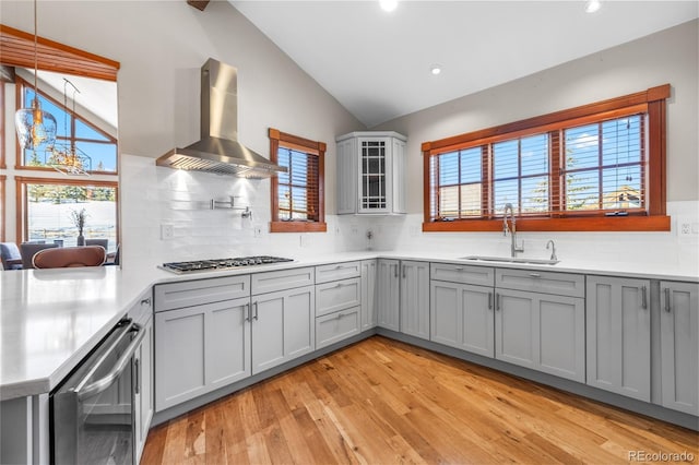 kitchen featuring stainless steel gas cooktop, lofted ceiling, gray cabinets, a sink, and wall chimney exhaust hood