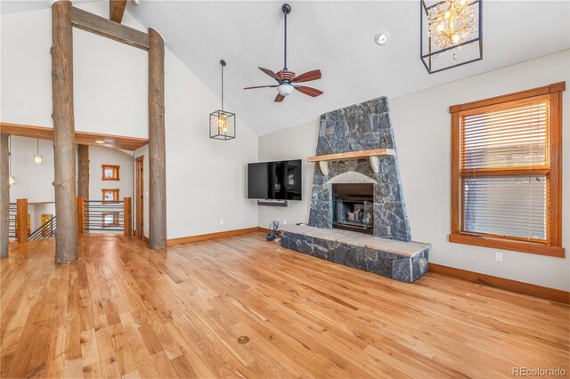 unfurnished living room with high vaulted ceiling, a ceiling fan, wood finished floors, a stone fireplace, and baseboards